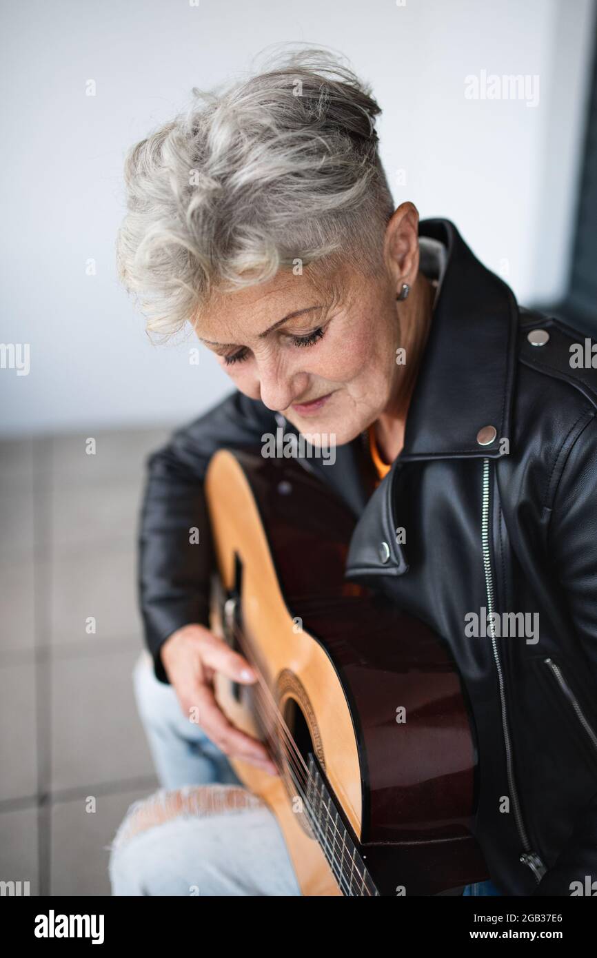 Ritratto di donna anziana seduta contro il backround nero, suonando la chitarra. Foto Stock