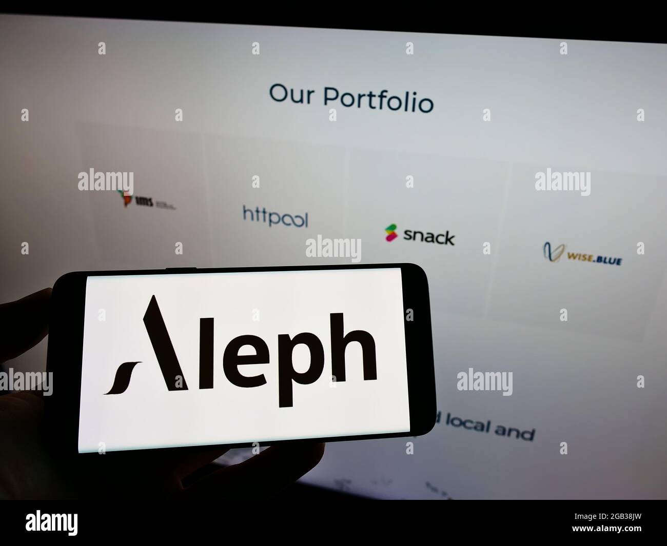 Persona che tiene il cellulare con il logo della società di media digitale statunitense Aleph Holding sullo schermo di fronte alla pagina web aziendale. Mettere a fuoco il display del telefono. Foto Stock