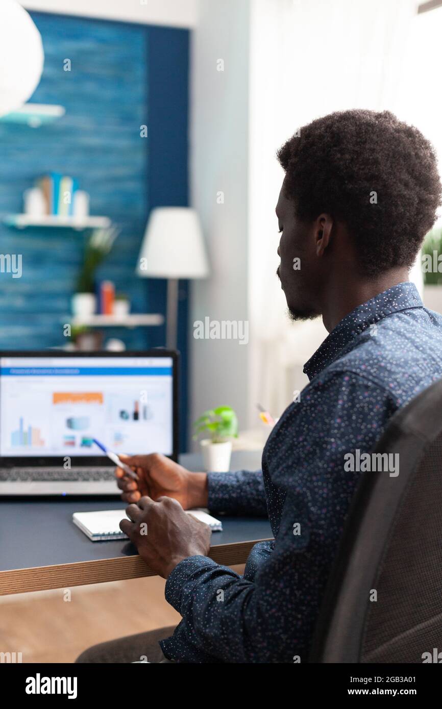 Uomo nero che lavora da casa utilizzando l'app dati dell'economia finanziaria su un notebook. African american guy utente di computer che usa il luogo di lavoro di affari internet online sito web di comunicazione stile di lavoro Foto Stock