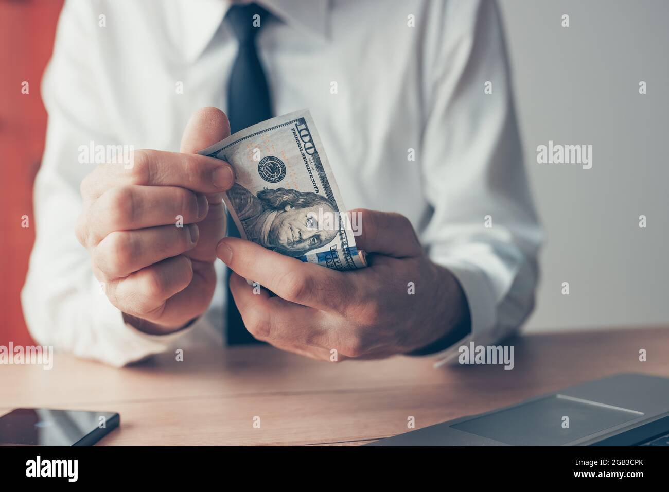 Uomo d'affari che conta denaro contante in dollari USA alla scrivania dell'ufficio, primo piano con la messa a fuoco selettiva Foto Stock