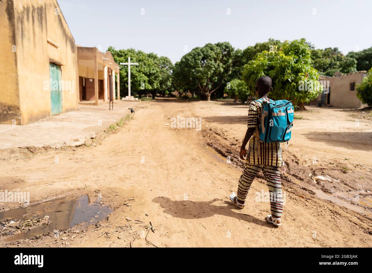 In questa immagine, un ragazzo nero solitario ben vestito con zaino blu sulla strada per la scuola domenicale o messa in un villaggio cristiano deserto in Africa Foto Stock