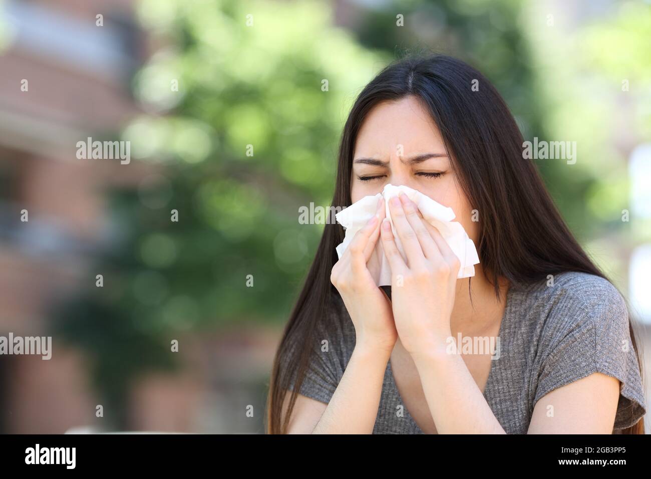 Donna asiatica malata che soffia su tessuto all'aperto in strada Foto Stock