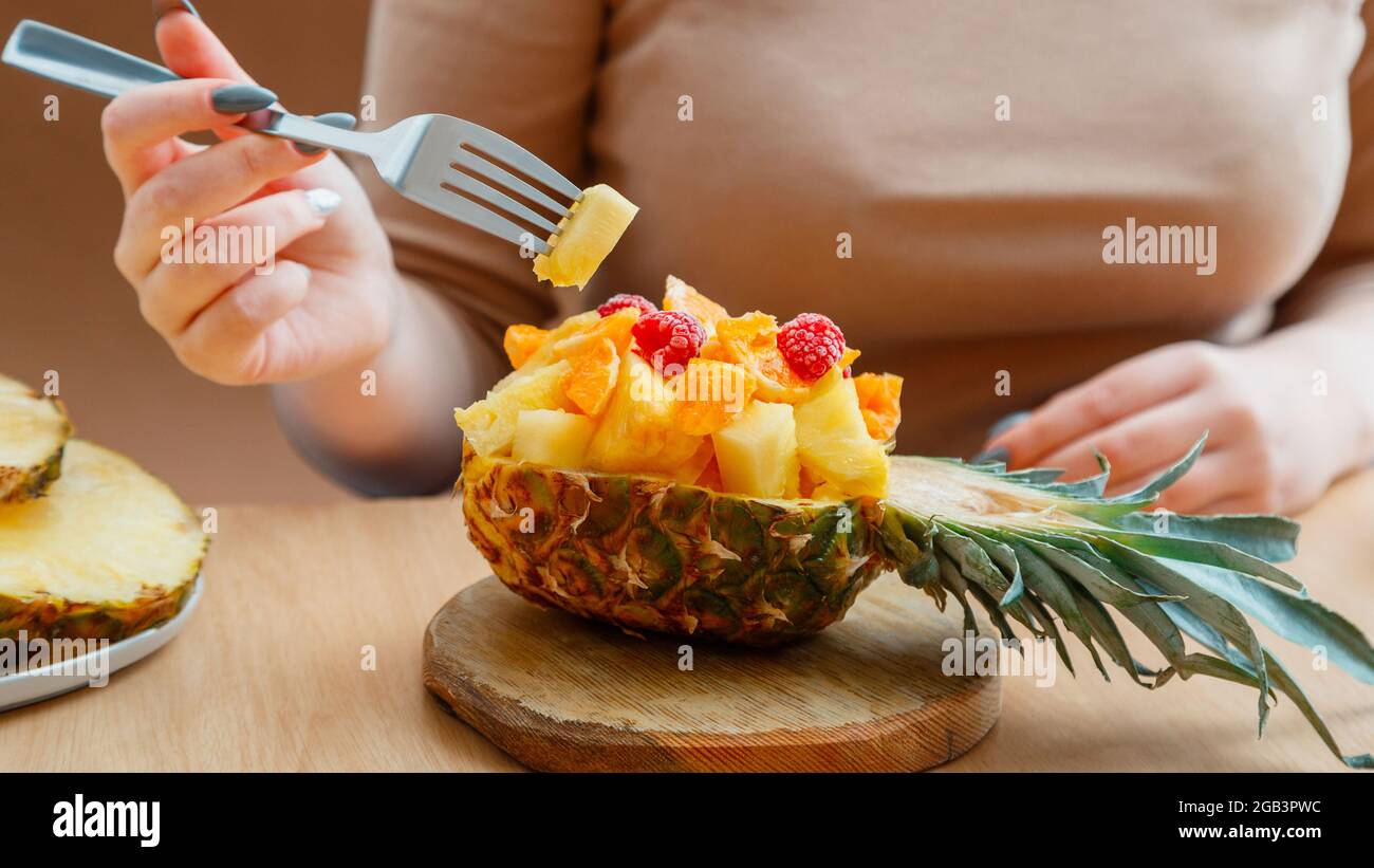 Macedonia di frutta in mezza ciotola di ananas. Gustosa insalata di frutta tropicale mangia donna nel caffè. Cibo frutta mix dessert servito sul tagliere in ananas. Lungo Foto Stock