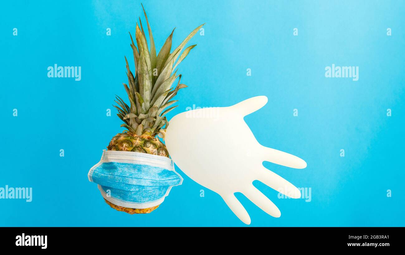 Ananas in maschera medica con guanto medico di gomma su sfondo blu. La frutta di ananas usa i prodotti di igiene personale durante la vacanza di corsa di estate Foto Stock