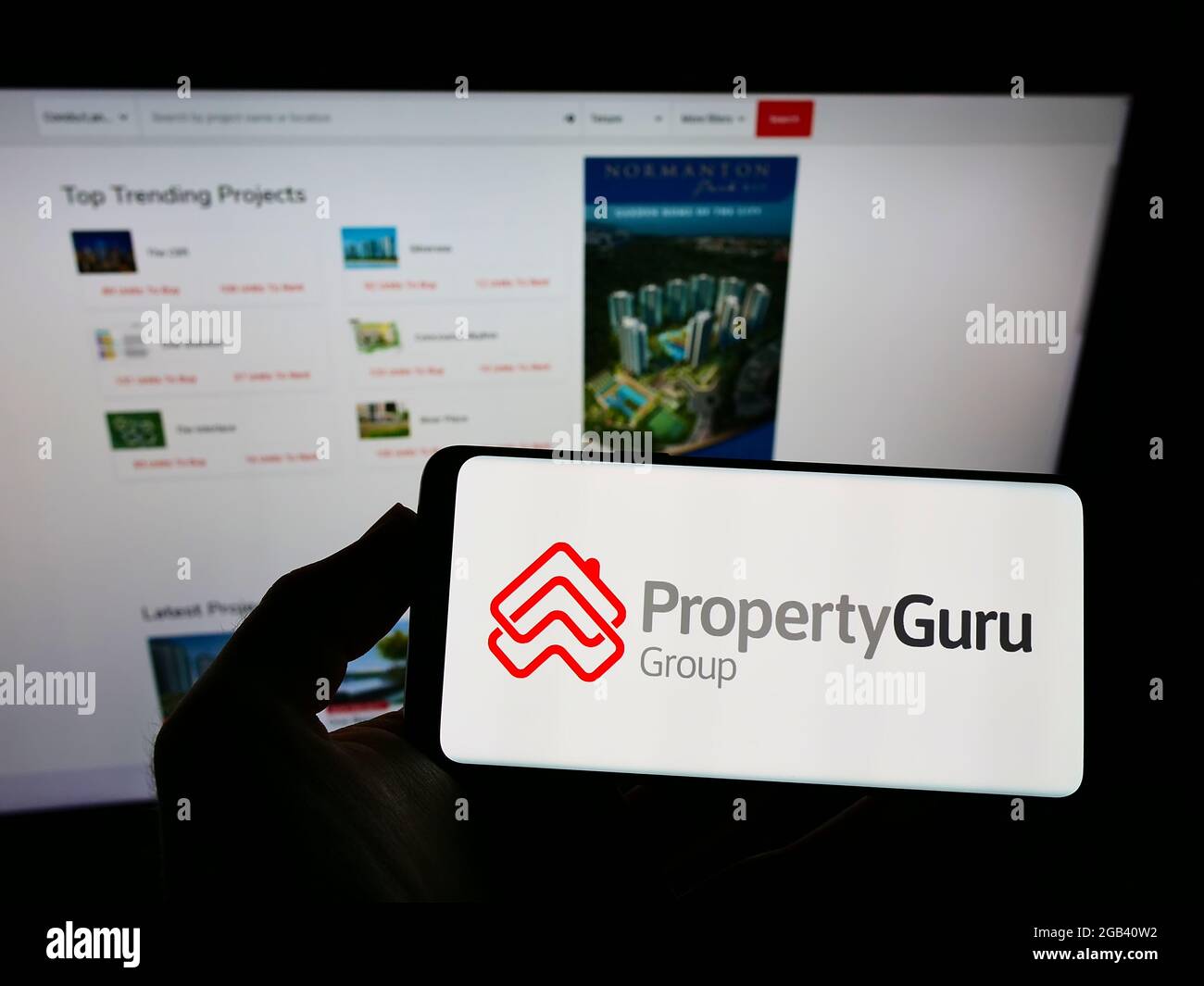 Persona che tiene il telefono mobile con il logo della società di proprietà online PropertyGuru Pte. Ltd. Sullo schermo davanti alla pagina web. Mettere a fuoco il display del telefono. Foto Stock