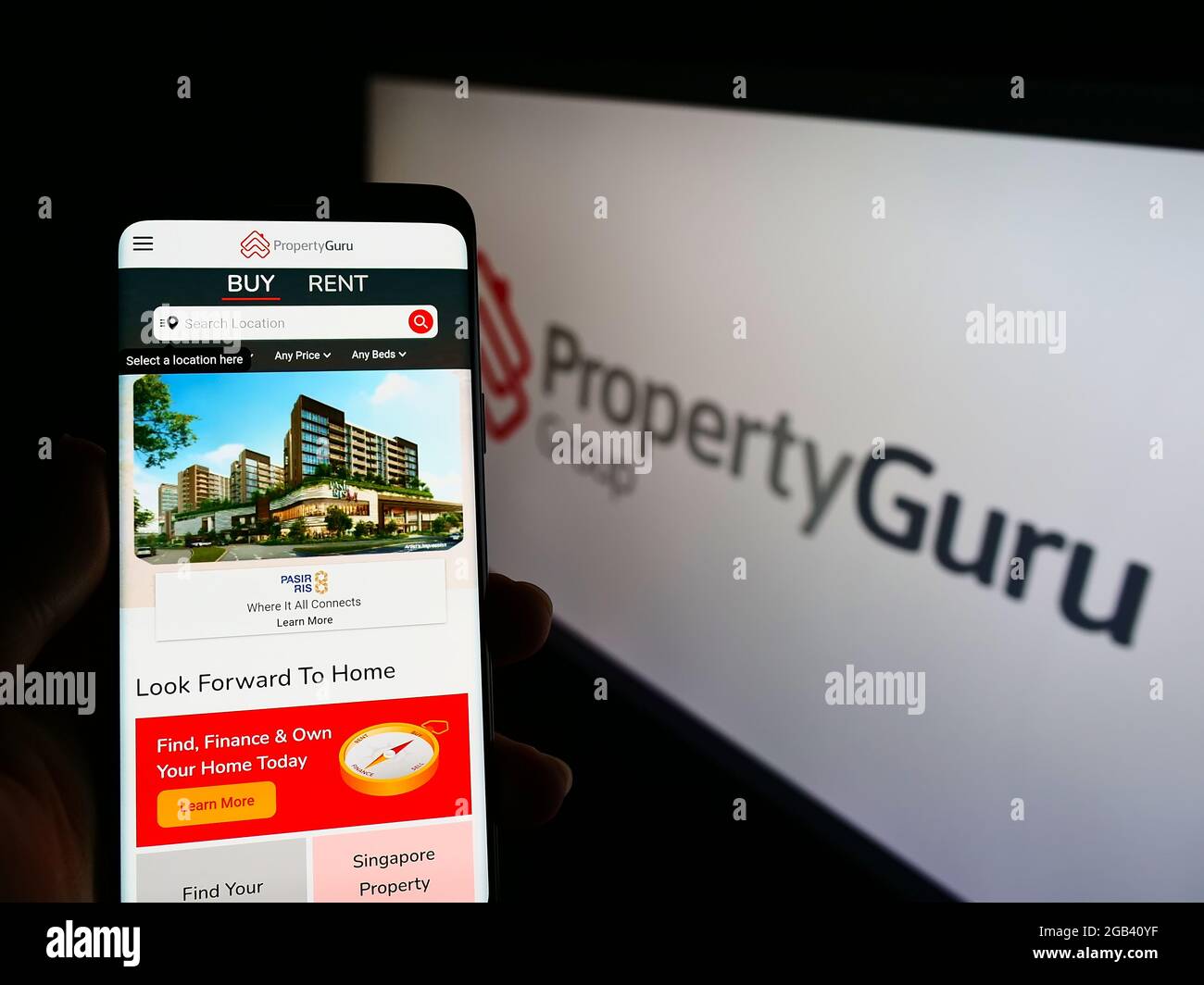 Persona che detiene smartphone con sito web della società di proprietà online PropertyGuru Pte. Ltd. Su schermo con logo. Mettere a fuoco il centro del display del telefono. Foto Stock