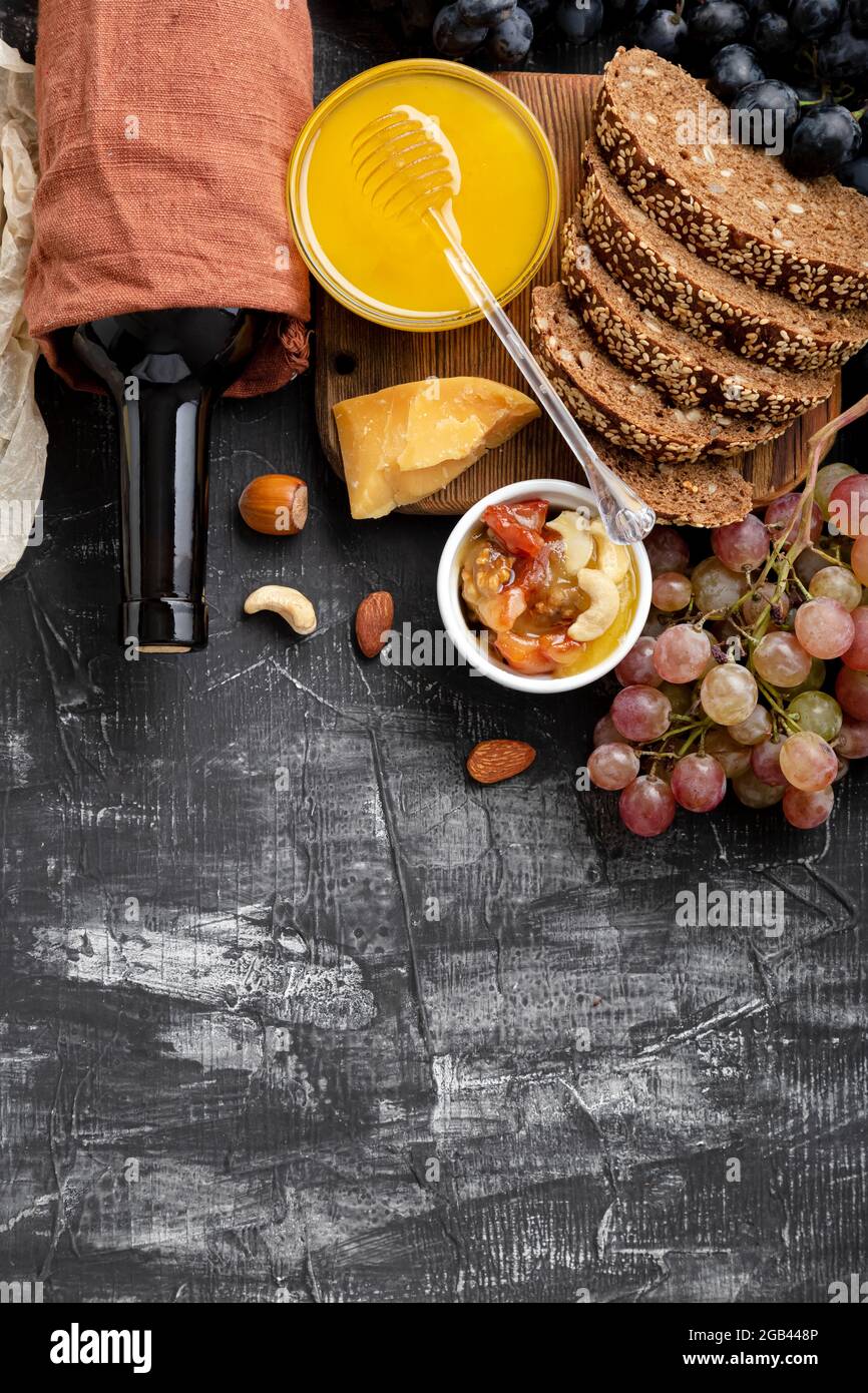 Bevande mediterranee a base di ingredienti per la cena. Vino miele formaggio noci snack pane uva frutta su fondo nero scuro pietra con spazio copia Foto Stock