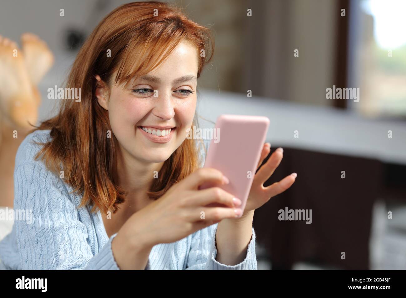 Donna felice sdraiata in camera da letto utilizzando lo smartphone a casa Foto Stock