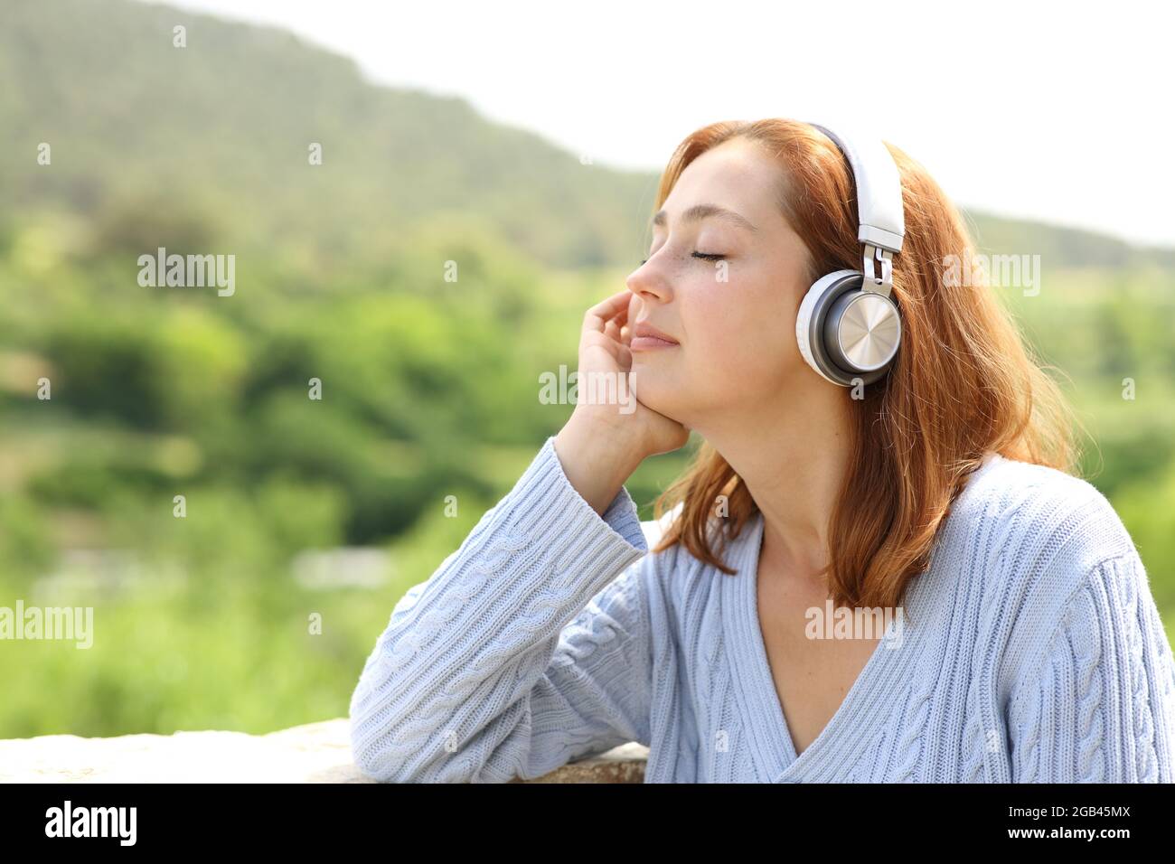 Donna che riposa ascoltando la musica con le cuffie wireless in natura Foto Stock