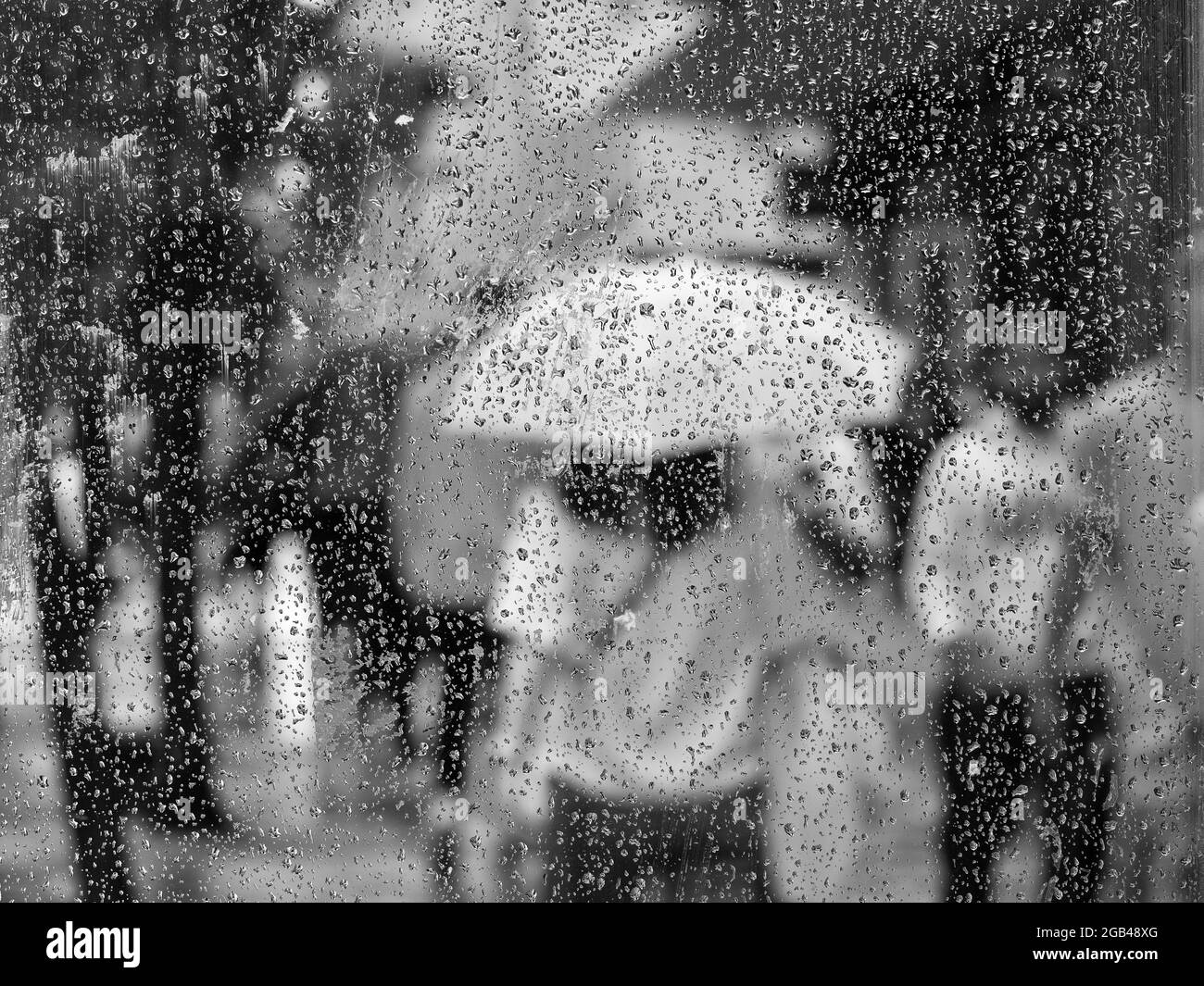 Le gocce di pioggia appaiono sul vetro come una figura fuori fuoco porta un ombrello durante il tempo bagnato a Londra. Foto Stock