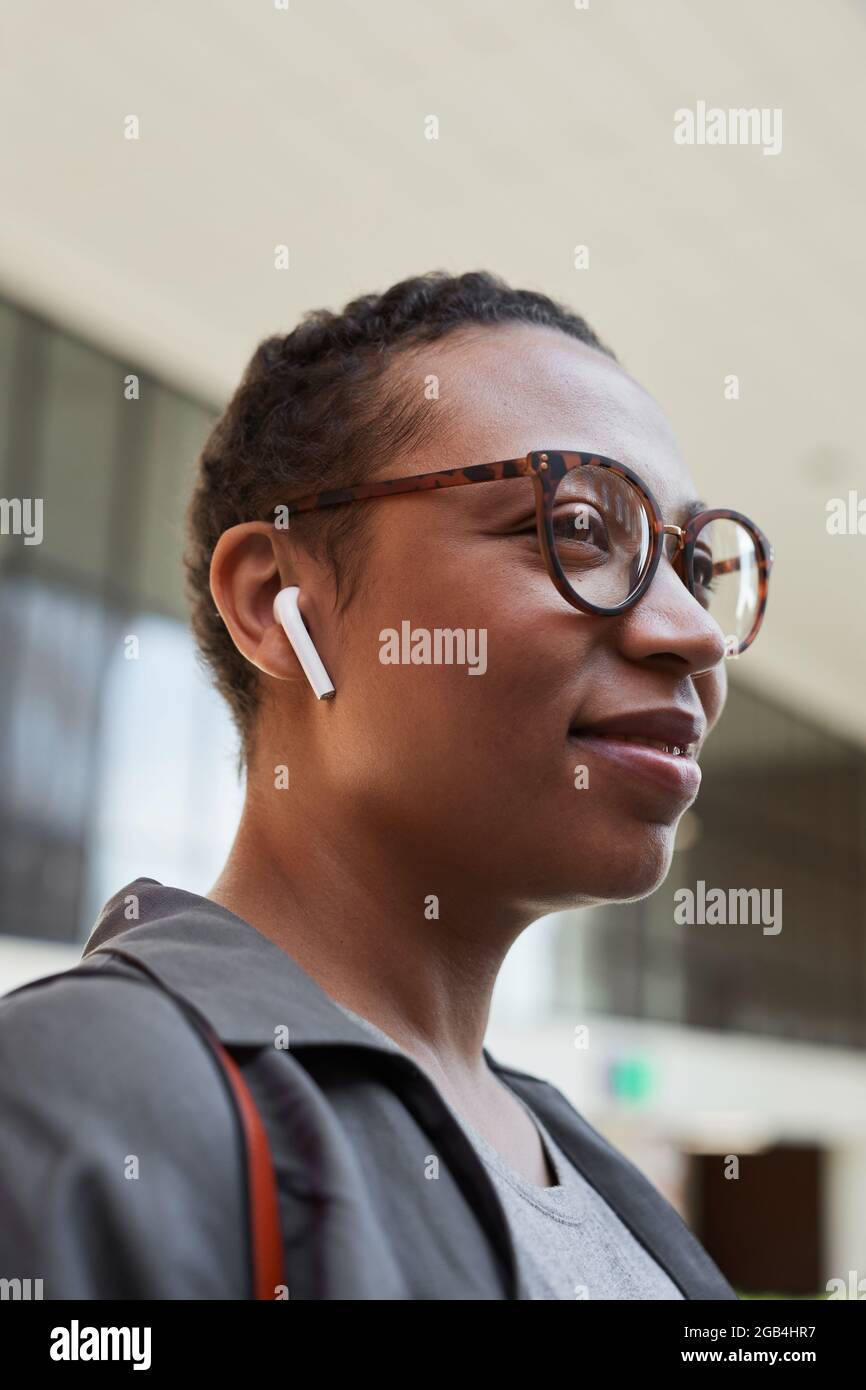 Giovane donna africana in occhiali che ascolta la musica con le cuffie senza fili camminando per la strada in città Foto Stock