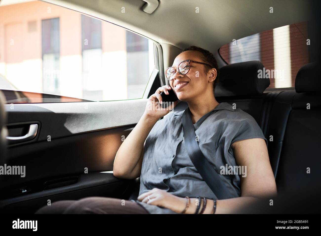 Felice donna africana seduta in macchina e sorridente durante la conversazione sul cellulare Foto Stock