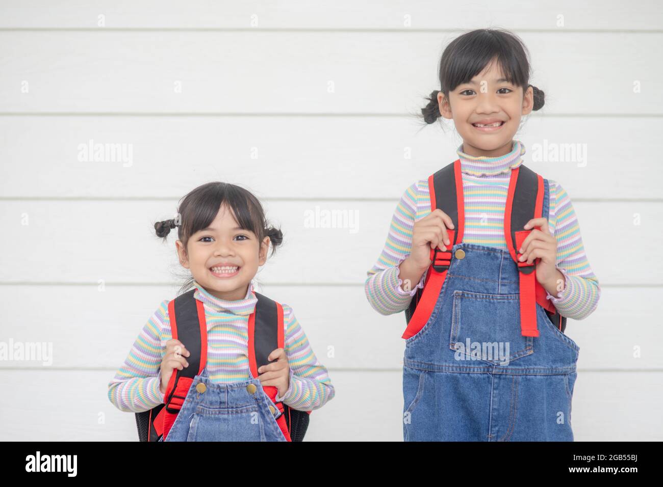 Ritorno a scuola. Due bambine asiatiche carine con borse da scuola che tengono insieme un libro su sfondo bianco Foto Stock