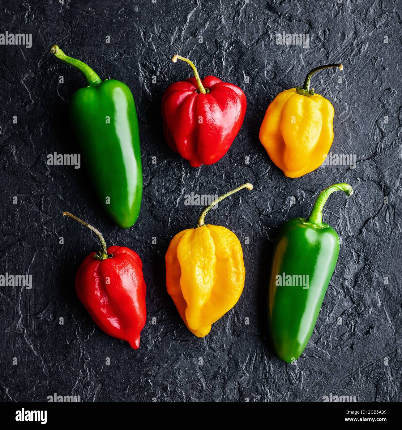 Diversi colori peperoni caldi jalapeno e habanero su fondo nero closeup. Fotografia alimentare Foto Stock