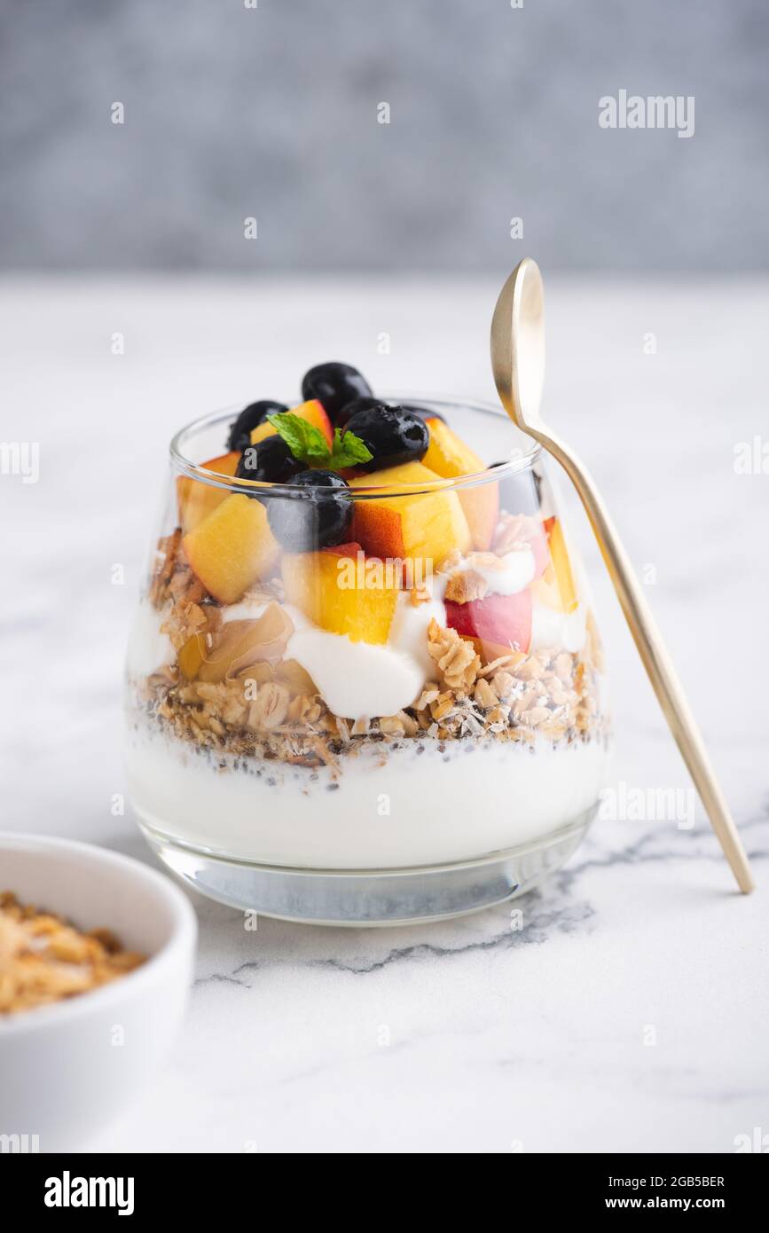 Yogurt greco con muesli e frutta in vaso su sfondo bianco di marmo, spazio copia. Cibo sano Foto Stock