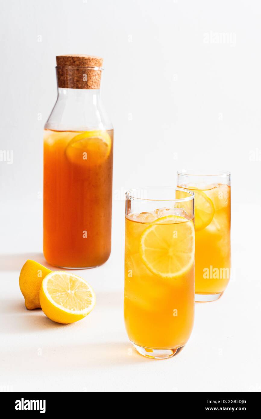 Due bicchieri e una caraffa di tè fresco freddo al limone su sfondo bianco. Foto Stock