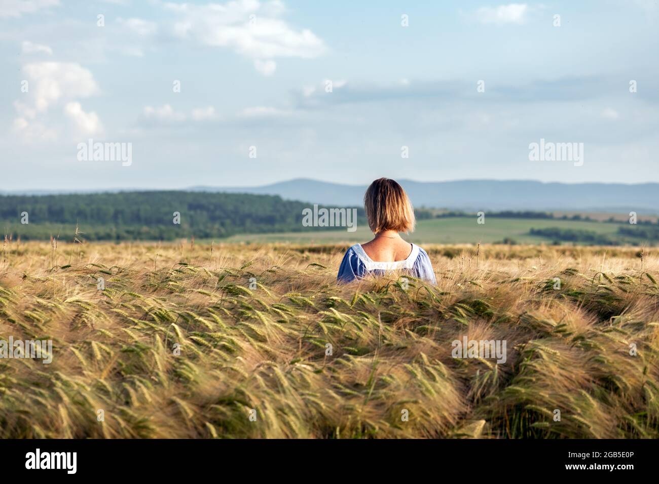 Donna in un campo di grano sullo sfondo del cielo blu con le nuvole Foto Stock