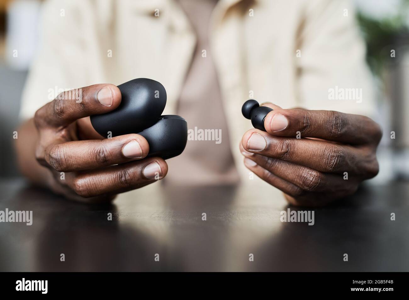 Primo piano di un uomo africano seduto al tavolo e aprendo la custodia con le cuffie wireless Foto Stock