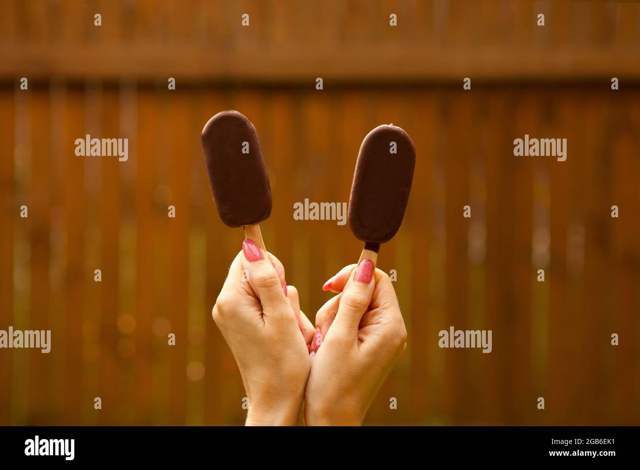cibo dolce estivo. mani femminili che tengono due gelato al cioccolato su sfondo marrone Foto Stock