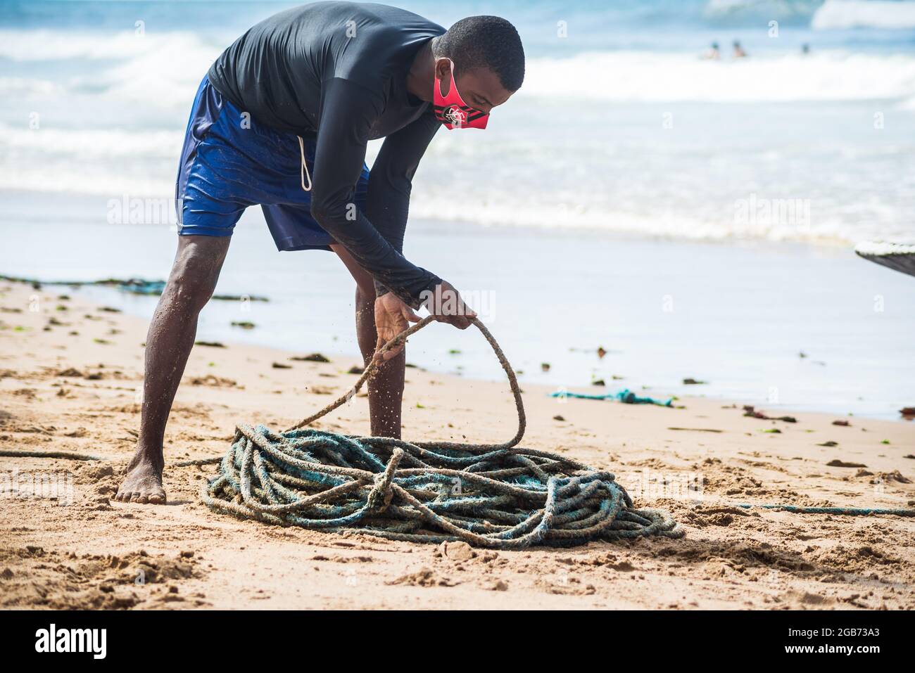 Salvador, Bahia, Brasile - 23 maggio 2021: Pescatore che rotola rete di pesca per immagazzinare in magazzino dopo la pesca sulla spiaggia di Boca do Rio. Foto Stock