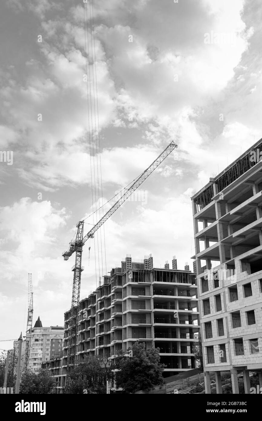 Foto in bianco e nero di un edificio residenziale a più piani in costruzione e gru su uno sfondo di cielo blu Foto Stock
