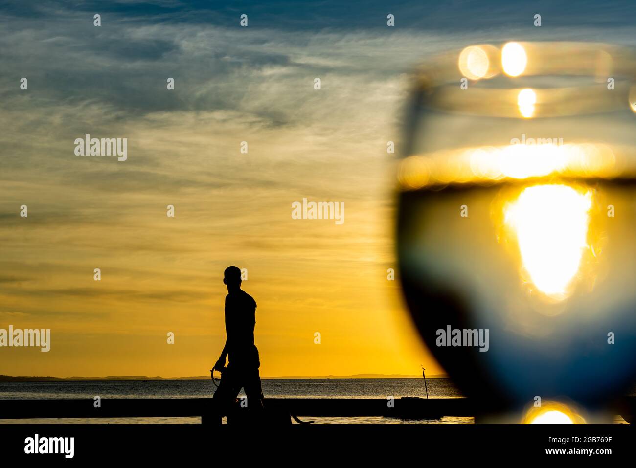 Salvador, Bahia, Brasile - 27 maggio 2021: Silhouette di persone che corrono, in bicicletta, a piedi, giocando al tramonto sulla spiaggia di Ribeira. In primo piano un vetro Foto Stock