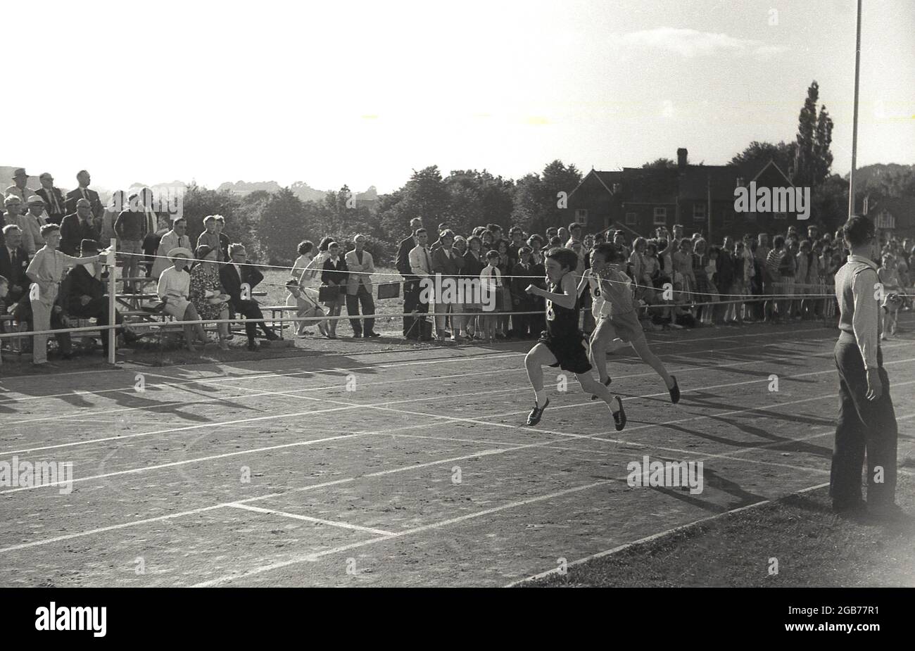 1964, storico, guardato dagli spettatori, due ragazzi adolescenti gareggiano in gara sprint running su una pista di scacchiera durante la giornata degli sport scolastici, con uno dei ragazzi che vince la gara mentre raggiunge per primo il traguardo, Exeter, Inghilterra, UK. Foto Stock