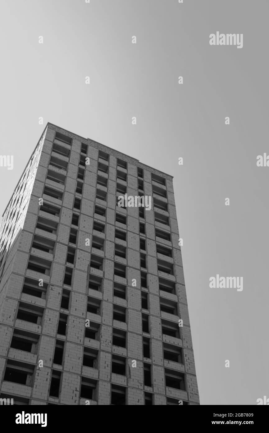 Foto in bianco e nero di un edificio residenziale a più piani in costruzione e gru su uno sfondo di cielo blu Foto Stock