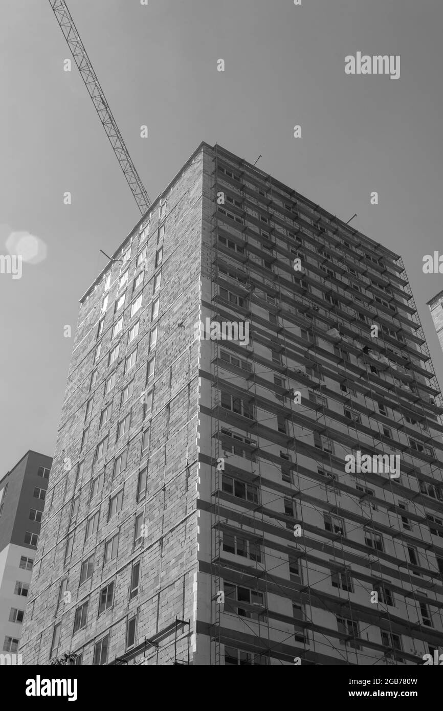 Foto in bianco e nero di un edificio residenziale a più piani in costruzione e gru su uno sfondo di cielo blu Foto Stock