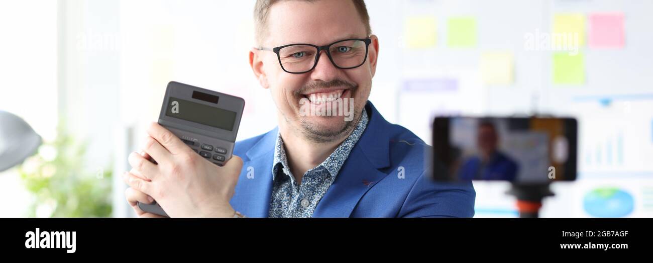 Un uomo d'affari sorridente tiene una calcolatrice e conduce corsi online su come aumentare i profitti Foto Stock