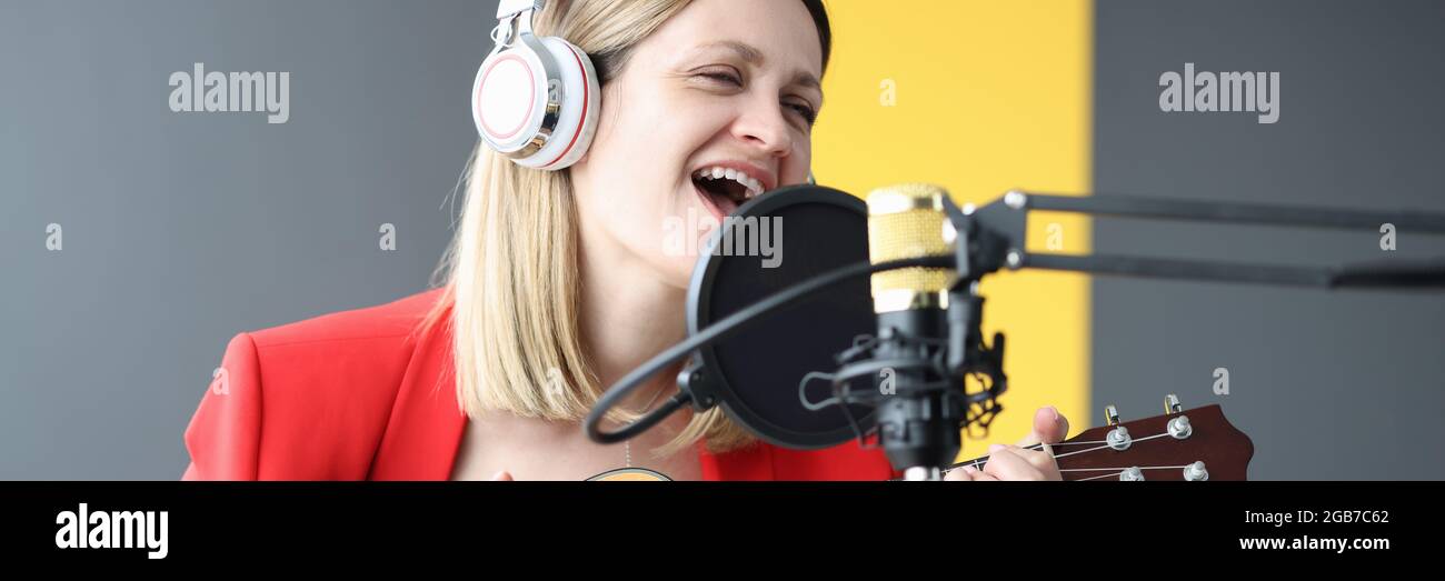 Donna canta e suona la chitarra con le cuffie davanti microfono Foto Stock
