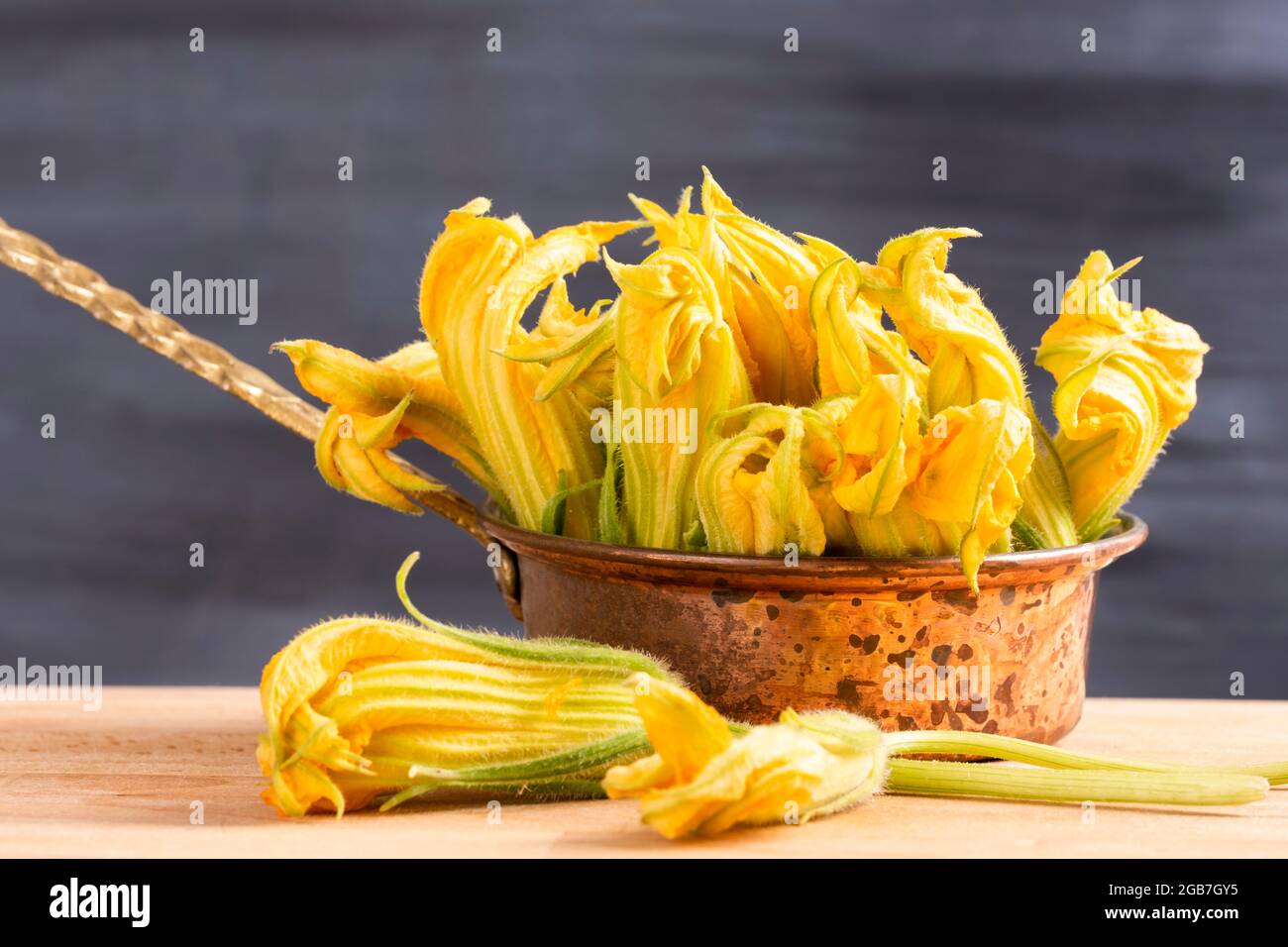 Concetto di fiori di zucca crudi commestibili: Fiori di zucca gialli freschi e biologici in vasetto di rame. Ingrediente sano dello stile di vita. Cucina mediterranea Foto Stock