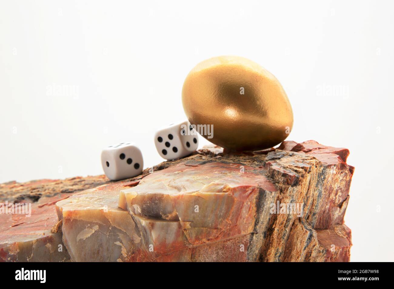 I dadi di gioco con l'uovo di nido d'oro sulla roccia si combinano in un avvertimento simbolico per evitare il rischio finanziario ad un uovo di nido d'investimento Foto Stock