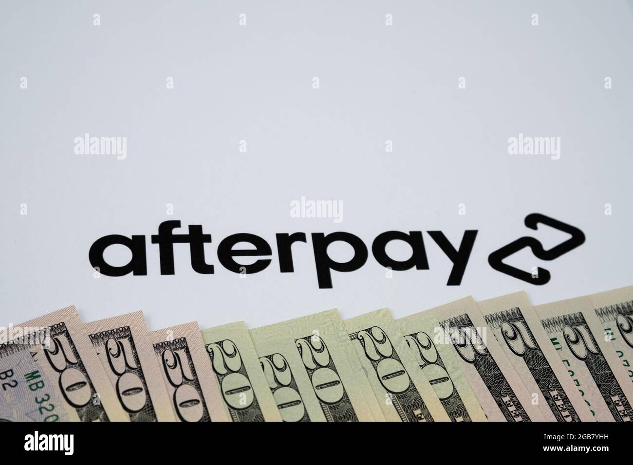 Bollette del dollaro e il logo della società Afterpay offuscato visto sfondo di carta. Servizio di prestito australiano. Stafford, Regno Unito, 2 agosto 2021. Foto Stock