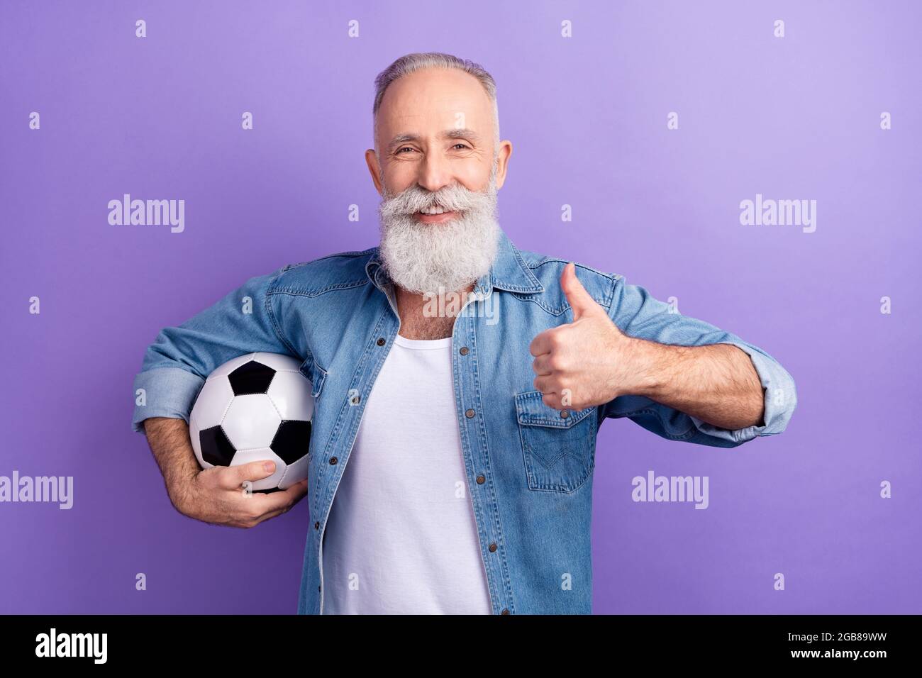 Foto di uomo anziano felice positivo sorriso tenere palla di calcio mostra pollice-up come fresco annuncio consiglio isolato su sfondo di colore viola Foto Stock