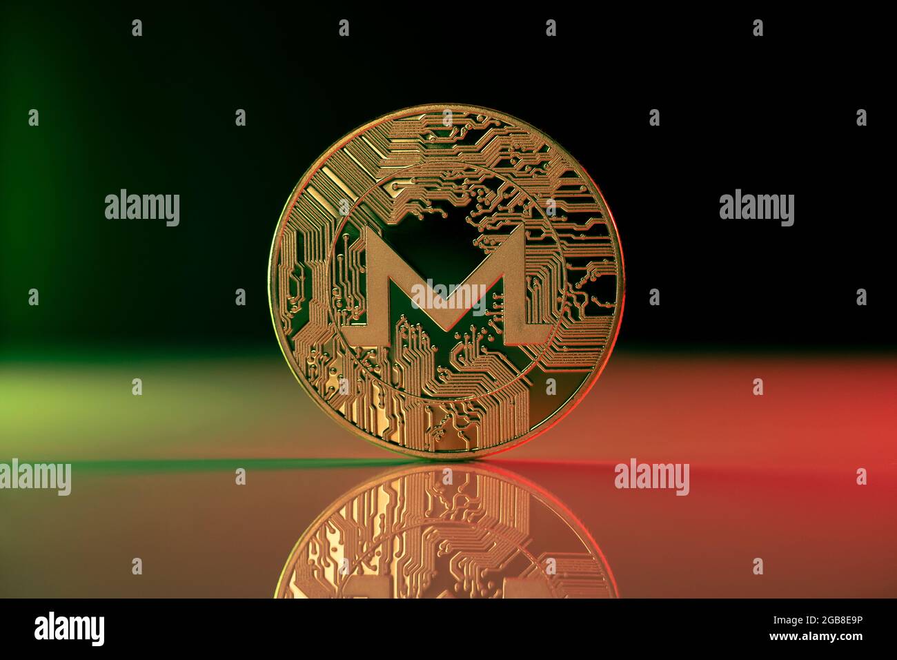 Moneta fisica di criptovaluta Monero XMR posta su superficie riflettente e illuminata con luci verdi e rosse Foto Stock