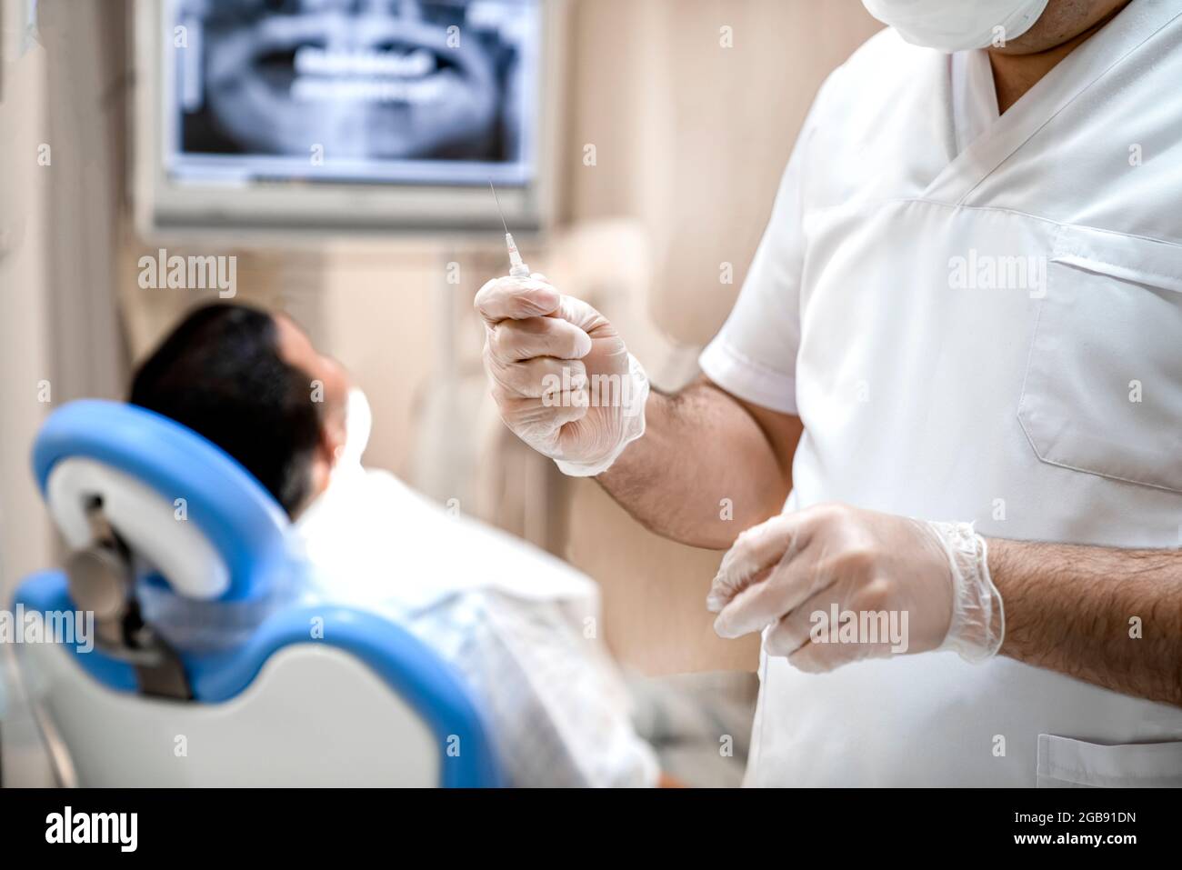 Il dentista tiene una siringa nelle mani con un farmaco per l'anestesia. Il paziente è in attesa di anestesia mentre è seduto sulla sedia del dentista. Foto Stock