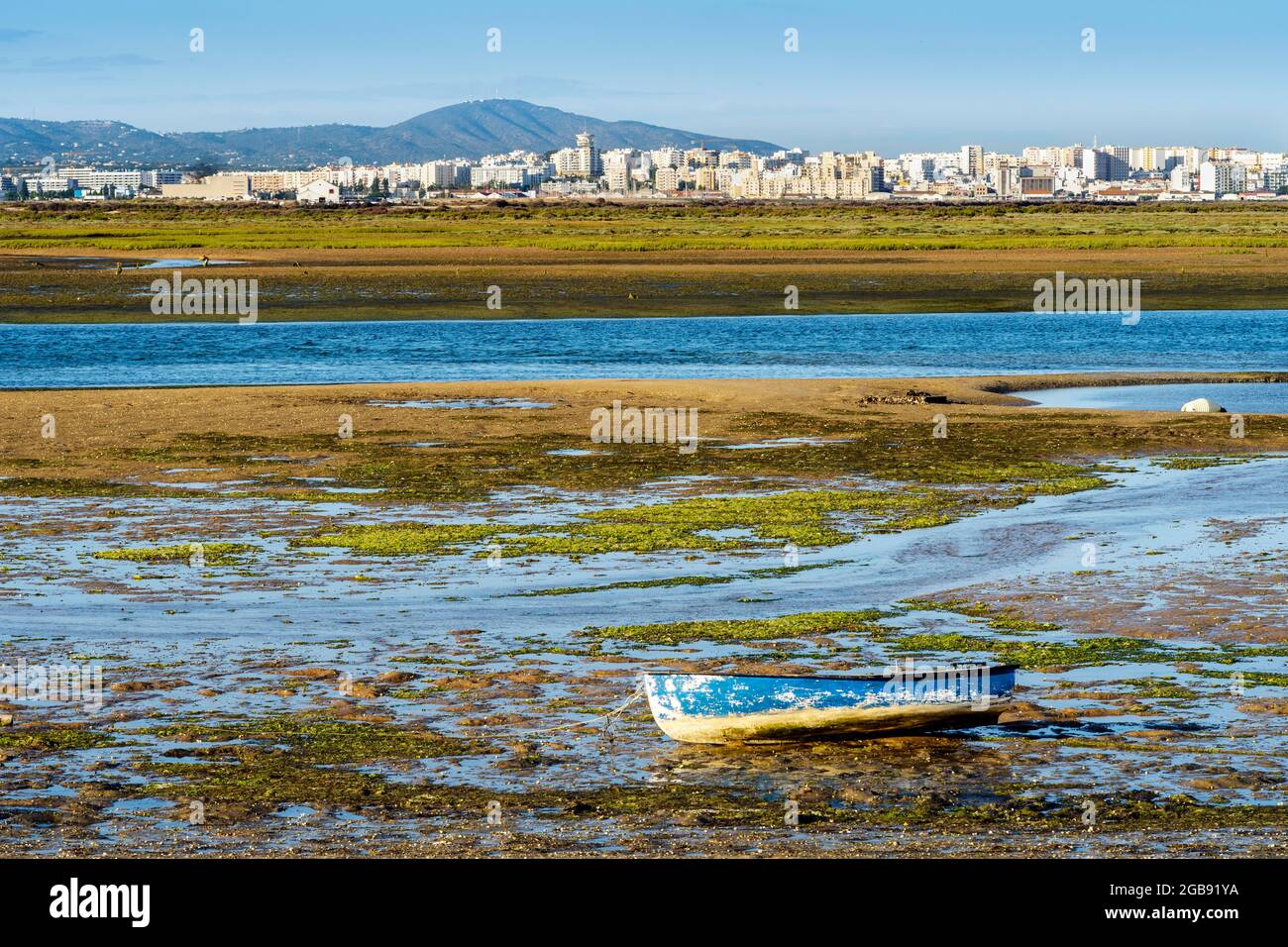 Barca di Ria Formosa zone umide durante la bassa marea, città di Faro sullo sfondo, Algarve, Portogallo Foto Stock