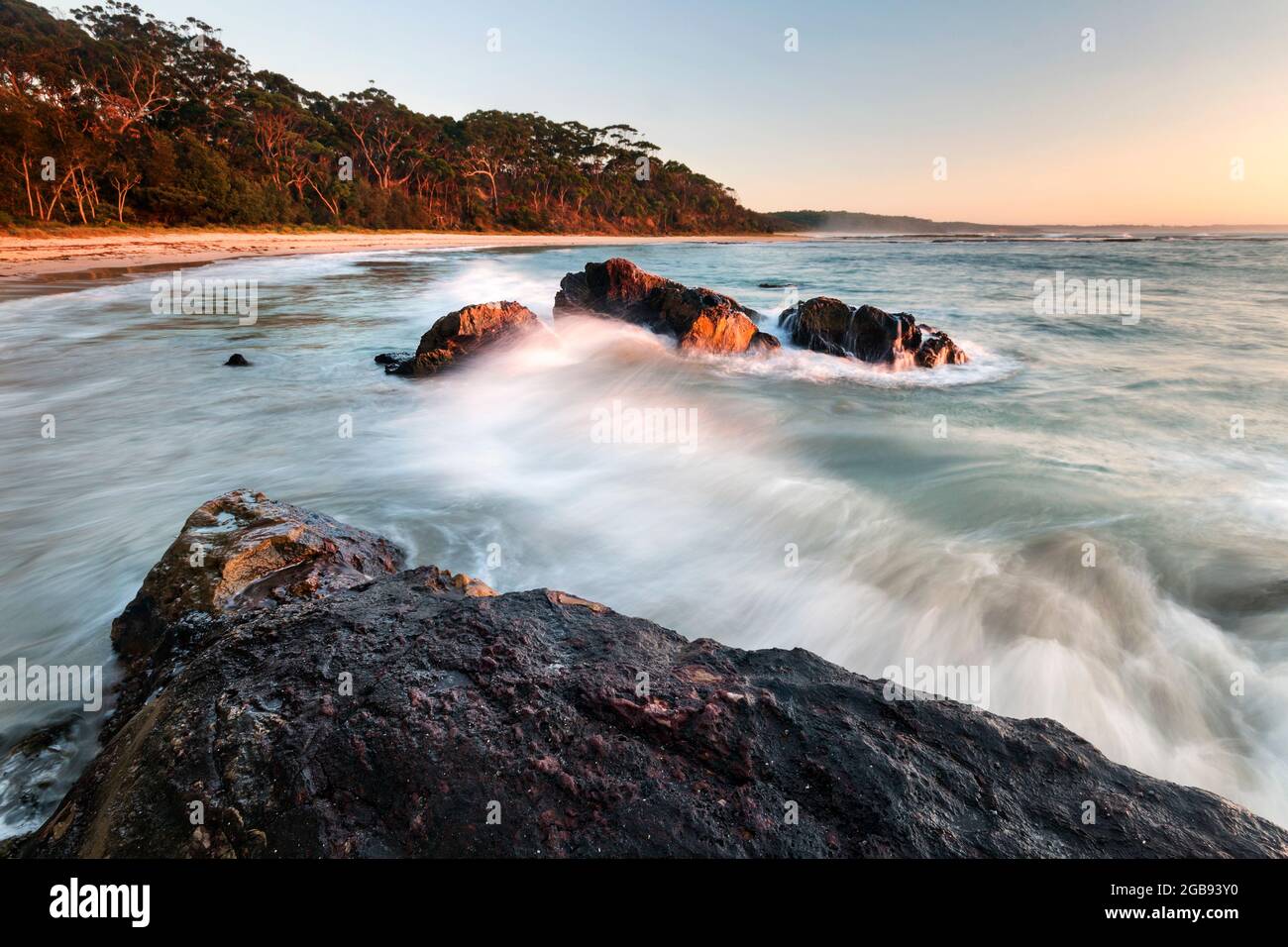 onde che colpiscono le rocce alla luce del mattino sulla spiaggia Foto Stock