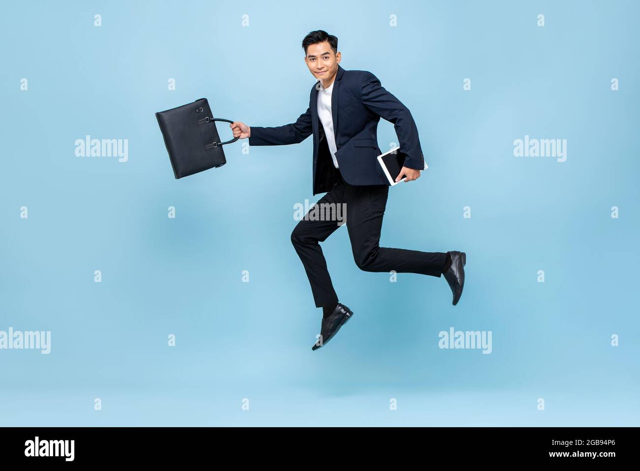 Ritratto a lunghezza intera di felice giovane bel lavoratore asiatico di ufficio maschile in esecuzione in borsa di tenuta a mezz'aria e libri in blu chiaro isolato studio backgroun Foto Stock