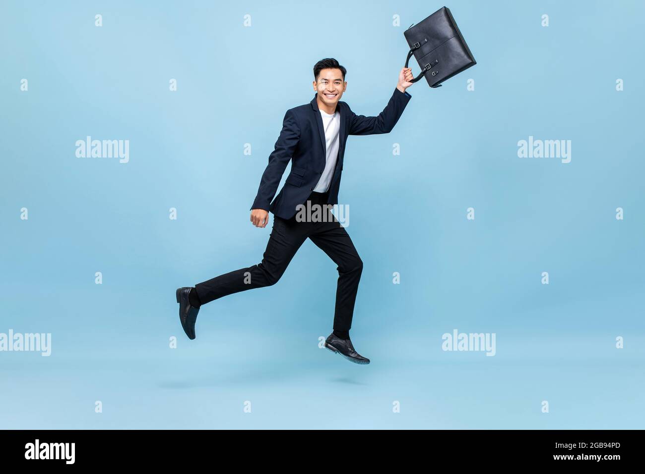Ritratto di sorridente giovane bel lavoratore asiatico maschile in ufficio che corre in mezzo-air borsa di tenuta in blu chiaro isolato sfondo studio Foto Stock