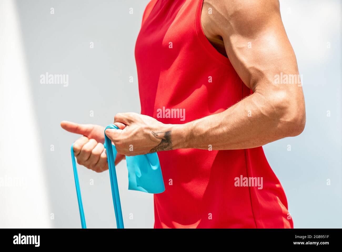 Calzare l'uomo sportivo muscolare facendo esercizio di ricciolo bicipite con resistenza banda all'aperto Foto Stock