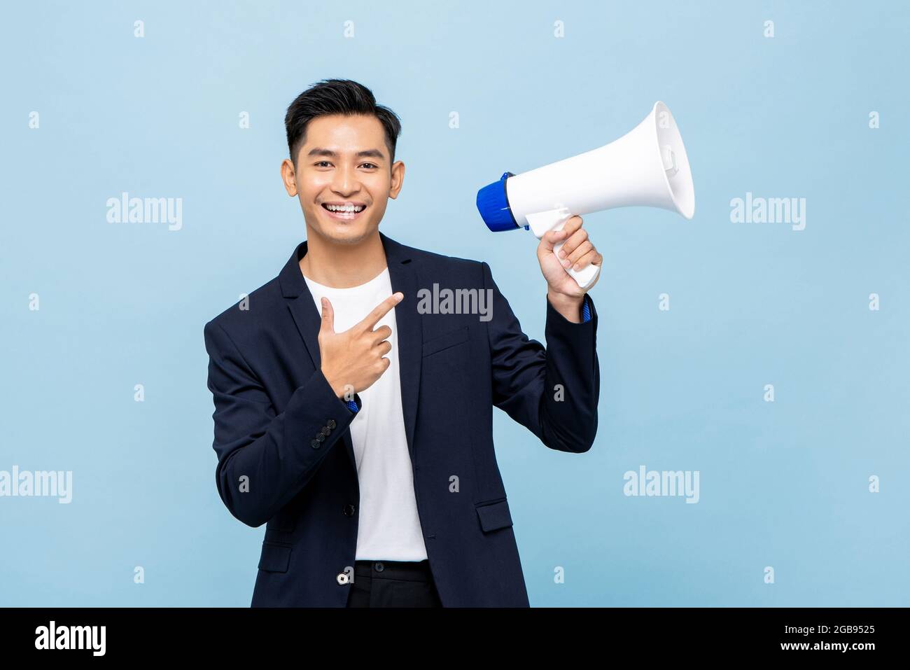 Sorridente bell'uomo asiatico che tiene isolato il megafono in azzurro sfondo Foto Stock