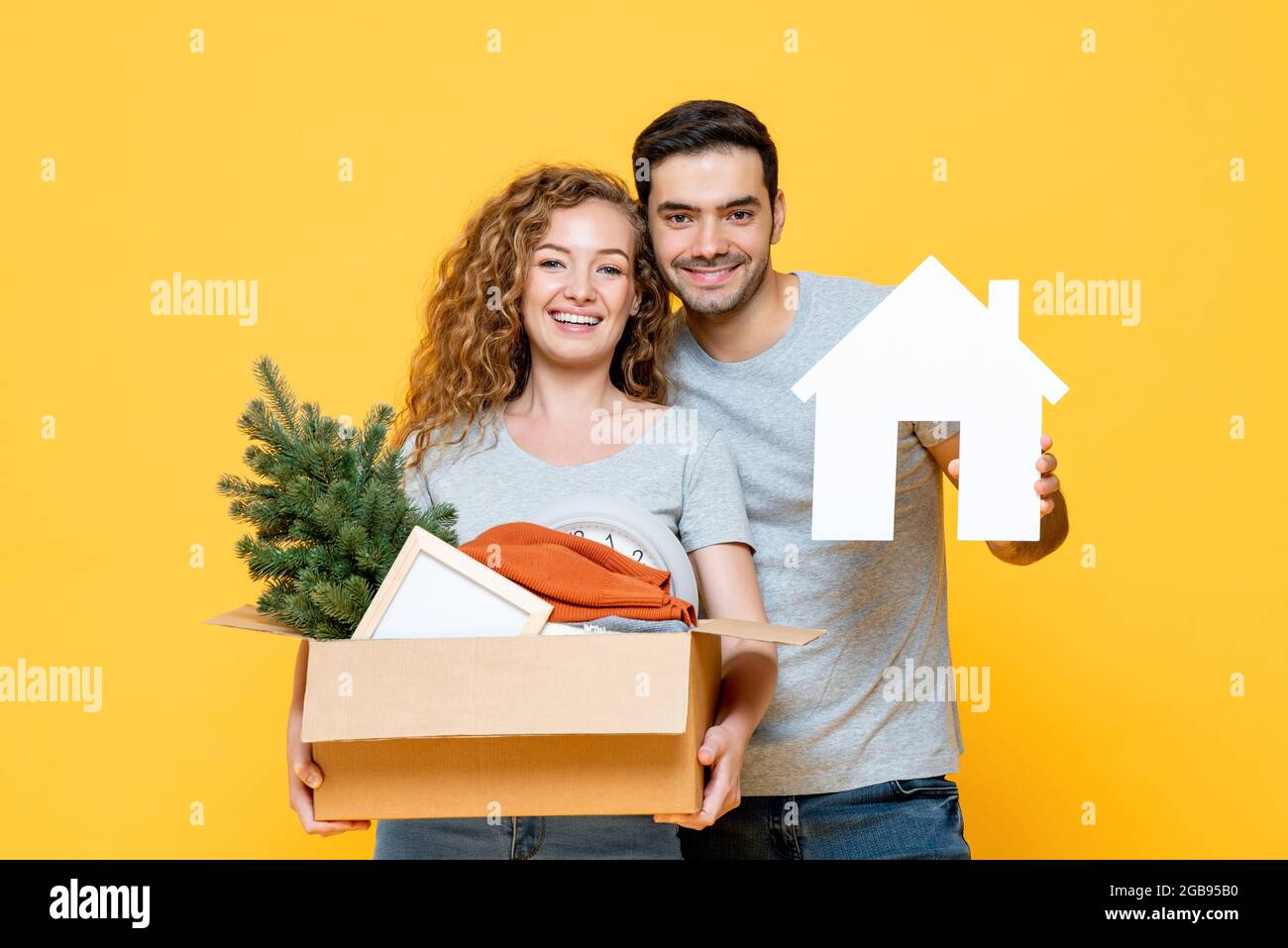 Giovani felici amanti interrazziali che portano il loro roba in giallo studio isolato sfondo, moving house concept Foto Stock