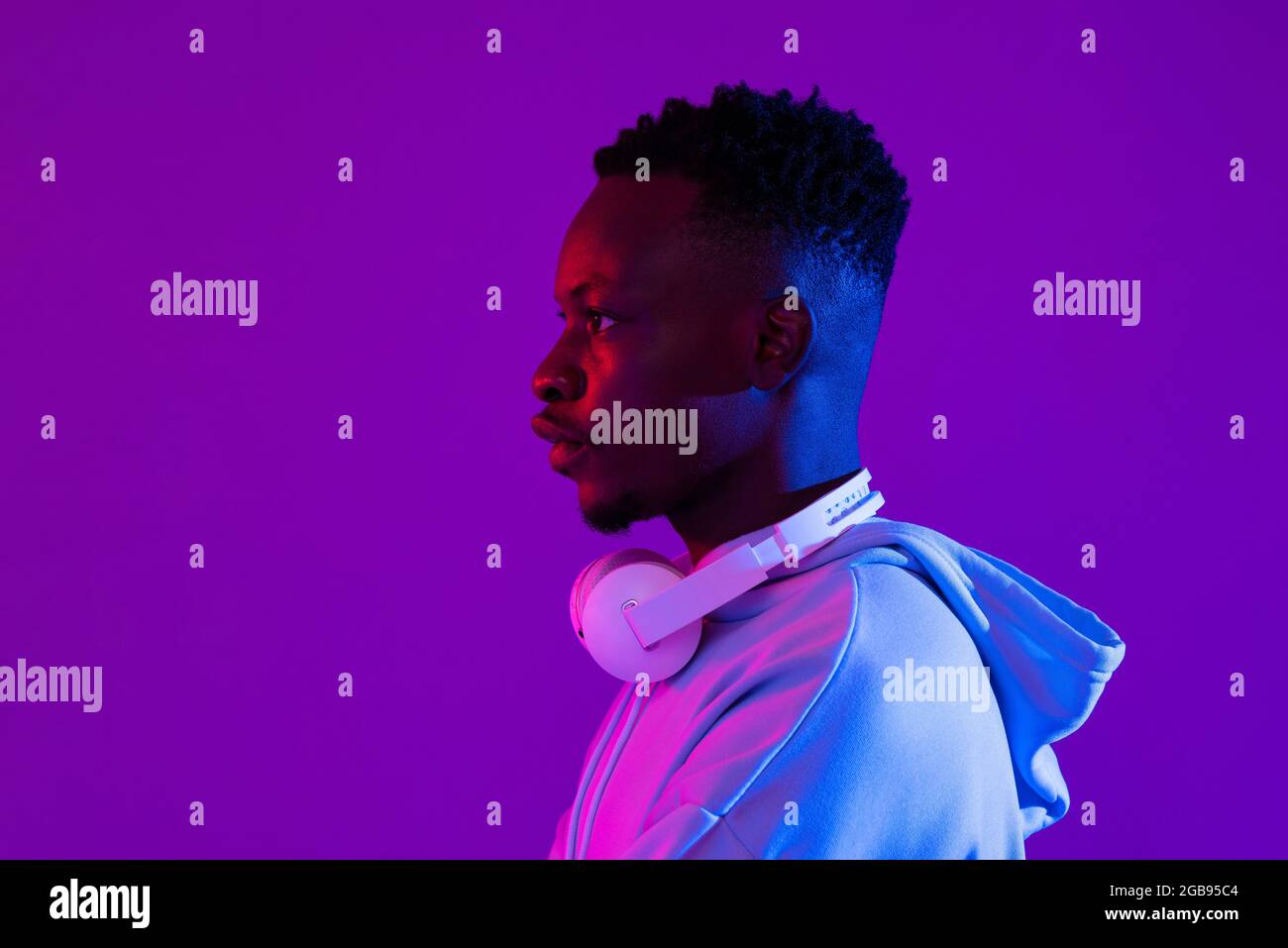 Ritratto con vista laterale di un giovane bel millenario africano con cuffie in viola futuristico neon light studio sfondo Foto Stock