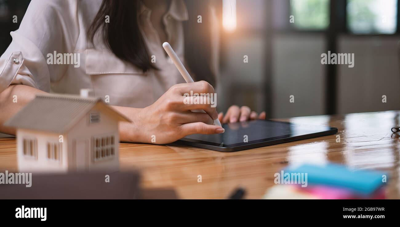 Donna architetto che utilizza un'applicazione tablet digitale per disegnare a mano una casa di design con un modello su una scrivania in legno. Idea di immobile in bene immobile. Foto Stock