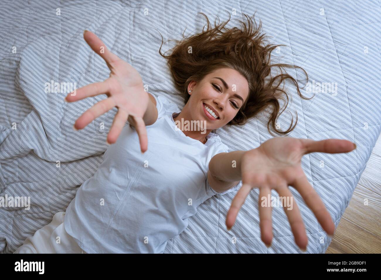 Concetto di mattina pigra. Bella donna felice si sveglia sdraiata a letto e allunga le braccia. Bella donna rilassante a casa in camera da letto. Foto Stock