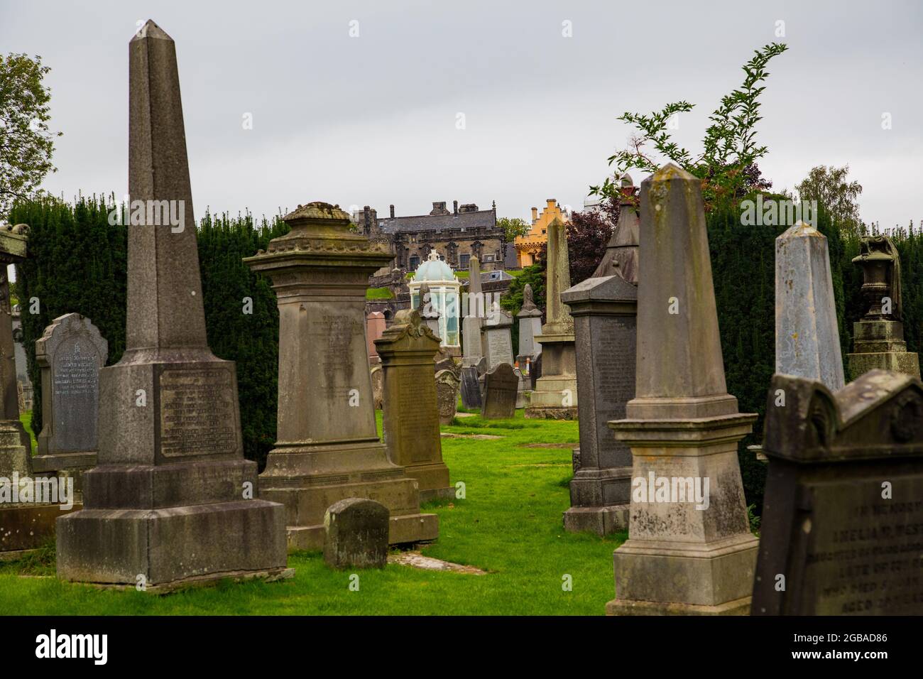 Cementerio de corte Gótico con lápidas en forma de piedra y monolitos, en prada con entrada de barrotes de hierro e iglesia detrás. Foto Stock