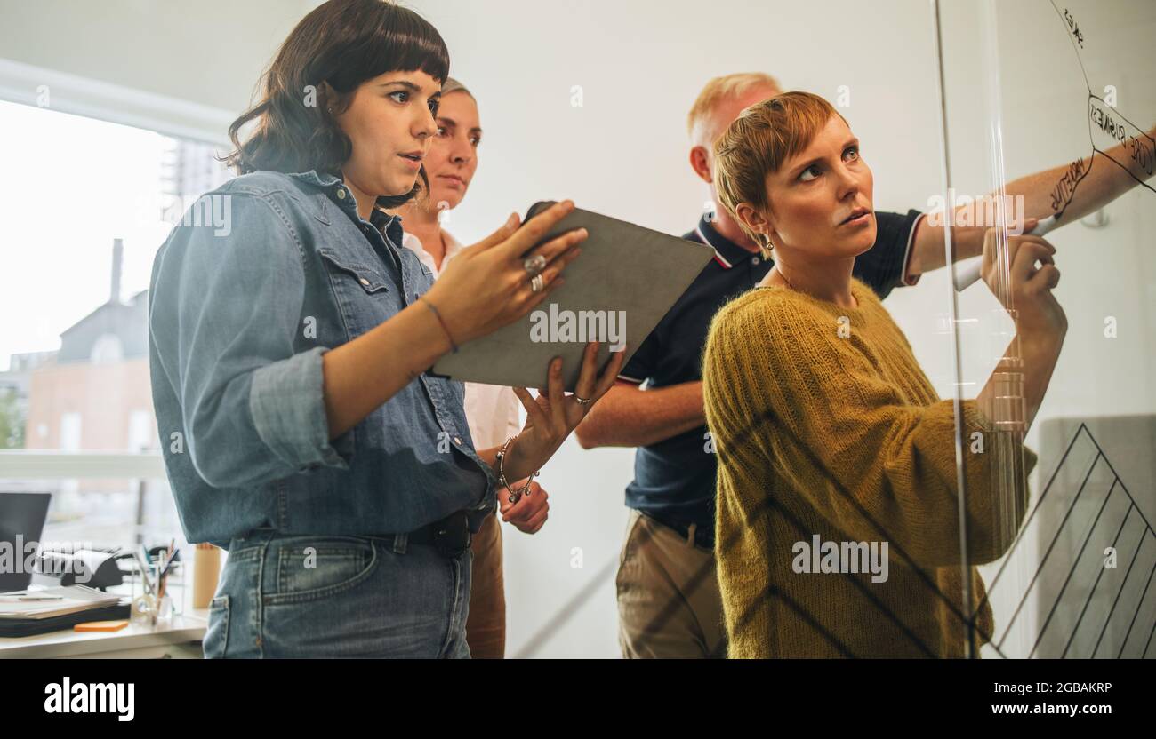 Il team sta progettando una nuova strategia aziendale sulla parete di vetro. Donna imprenditore che scrive sulla parete di vetro e che discute le sue idee con la squadra. Foto Stock