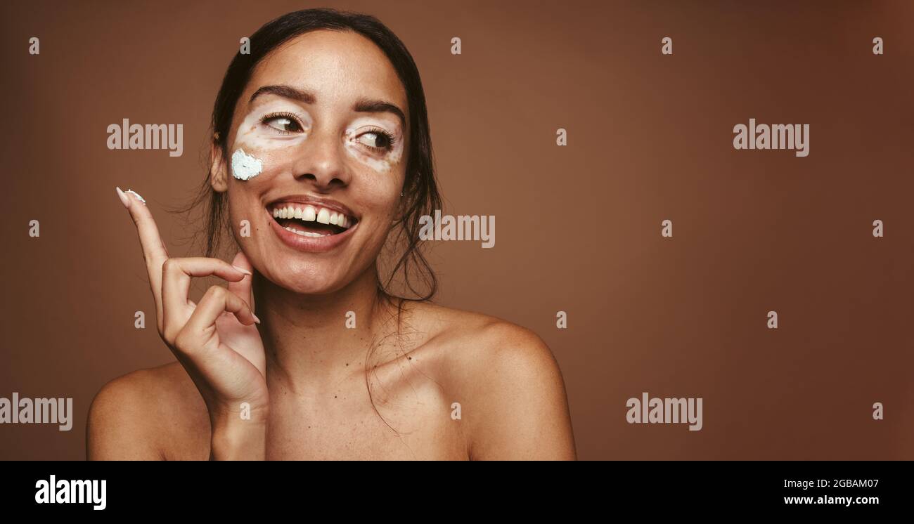 Donna sorridente che applica la maschera facciale. Primo piano di una giovane donna che applica il prodotto per la pelle. Foto Stock